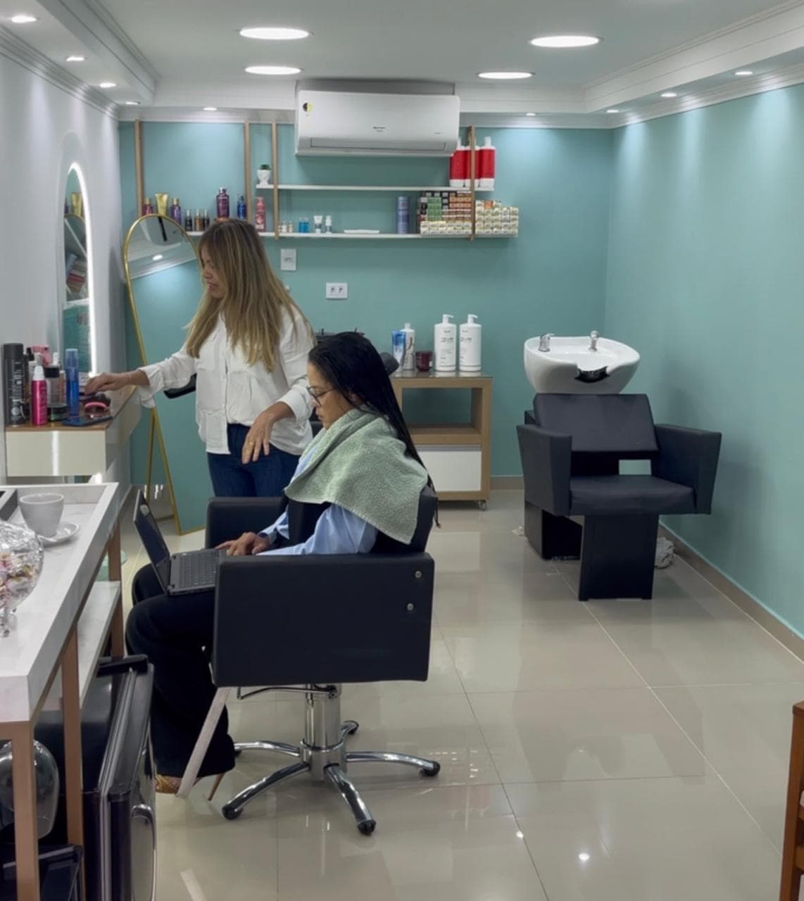 Cabeleireira atendendo uma cliente no salão de parede turquesa