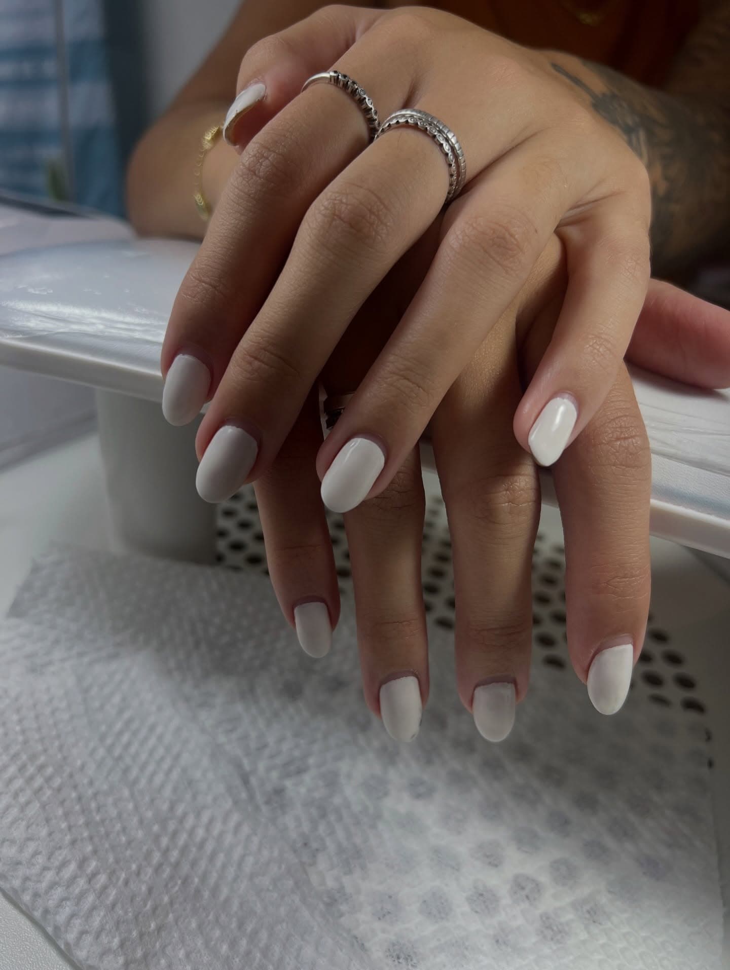 Unhas brancas com anéis prateados, sobre o apoio da manicure