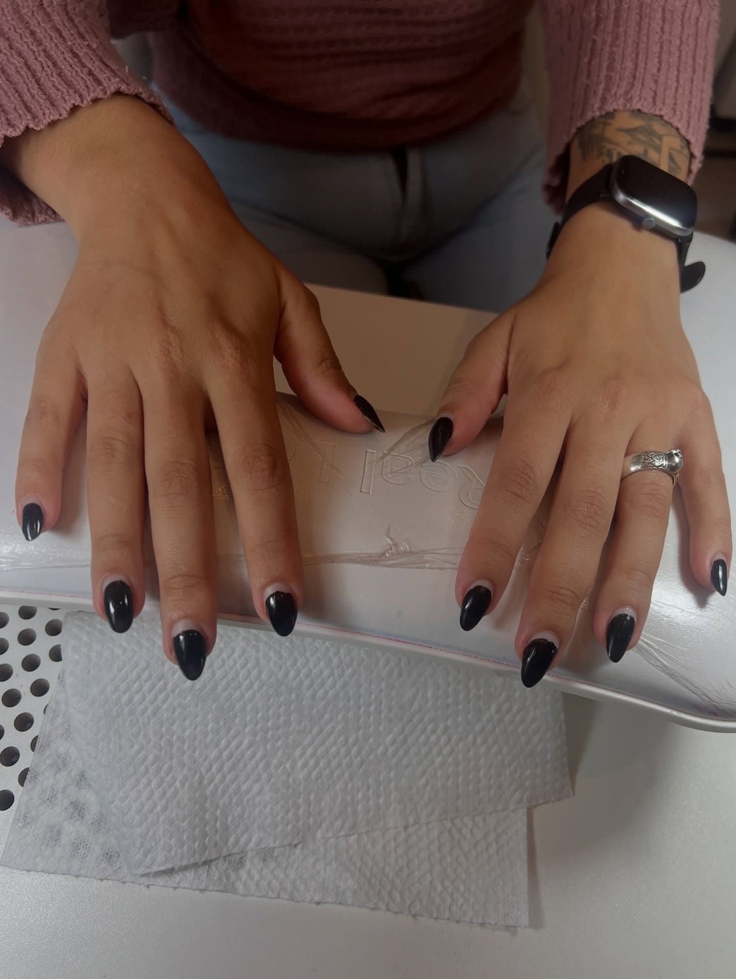 Mãos com unhas pretas curtas apoiadas na almofada da manicure